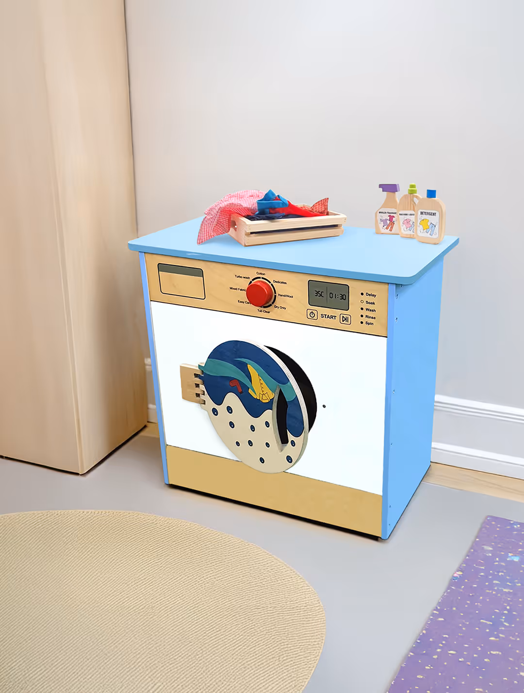 Toy washing machine with a blue top, beige front, and a round door featuring cartoon fish, with a laundry basket and detergent bottles on top.